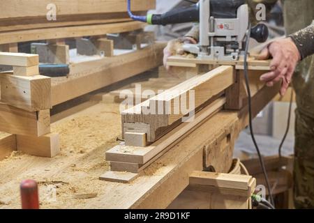 Zimmermannsfräsen Holzhandlauf mit Handfräsmaschine im Werkstattbereich. Handwerker verarbeitet Holzstücke mit einem elektrischen Instrument Stockfoto