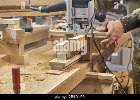 Zimmermannsfräsen Holzhandlauf mit Handfräsmaschine im Werkstattbereich. Handwerker verarbeitet Holzstücke mit einem elektrischen Instrument Stockfoto