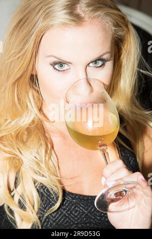 Eine Frau mit grünen Augen, die vor der Kamera über ein großes Glas Weißwein guckt Stockfoto
