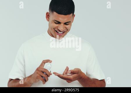 Ein glücklicher junger Mann, der sich eine Gesichtswäsche an die Finger legt und sich darauf vorbereitet, das Schönheitsprodukt auf sein Gesicht aufzutragen. Ein junger Mann, der einen gesunden und feuchtigkeitsspendenden Ski hinzufügt Stockfoto