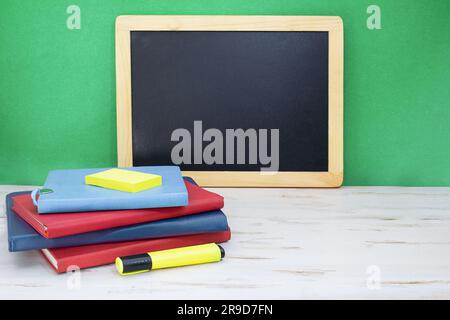 Stapel Notizblöcke mit Markierung auf weißem Tisch. Schwarzes Brett auf grünem Hintergrund. Zurück in die Schule. Speicherplatz kopieren Stockfoto