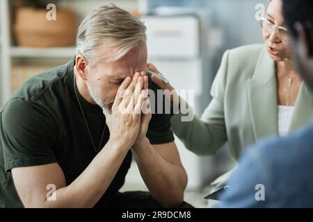 Konzentrieren Sie sich auf gestressten, grauhaarigen Mann, der sein Gesicht bedeckt, während er an einem posttraumatischen Syndrom leidet, nachdem er nach dem Krieg nach Hause zurückgekehrt ist Stockfoto