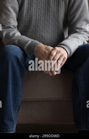 Nahaufnahme, vertikaler Schuss, unbekannter älterer Mann sitzt auf der Couch Stockfoto