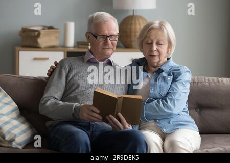 Fokussierte, reife Ehepartner, die zu Hause zusammen ein Buch lesen Stockfoto