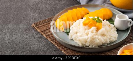 Köstlicher klebriger Reis aus thailändischer Mango mit geschnittenen frischen Mangofrüchten auf einem Teller mit grauem Tischhintergrund. Stockfoto