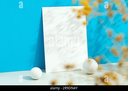 Leeres weißes Papiermodell auf blauem Hintergrund. Blumen im Vordergrund, Unschärfe. Stockfoto