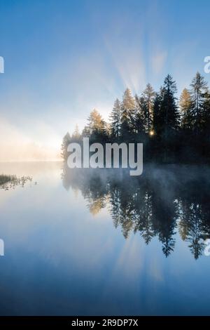 Sonnenaufgang über dem ruhigen Moorlandsee Etang de la Gruere im Kanton Jura, Schweiz Stockfoto
