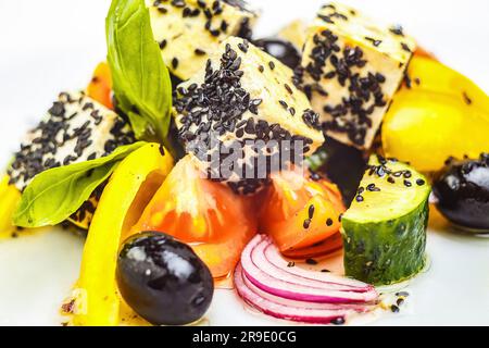 Ein lebendiges, gesundes Gericht aus frischen Produkten - Tomaten, Gurken, Orange und Basilikum - garniert mit schwarzen Sesamsamen und Oliven. Perfekt für Ihr Wohlbefinden! Stockfoto
