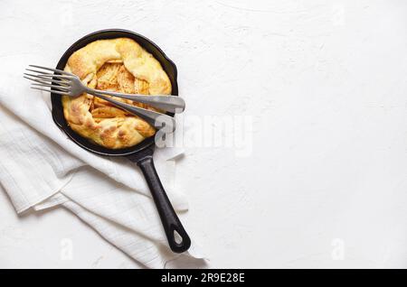 Apfelgalette in einer schwarzen Pfanne mit zwei Gabeln und einem Stück weißem Tuch auf weißem Hintergrund mit Kopierraum. Stockfoto