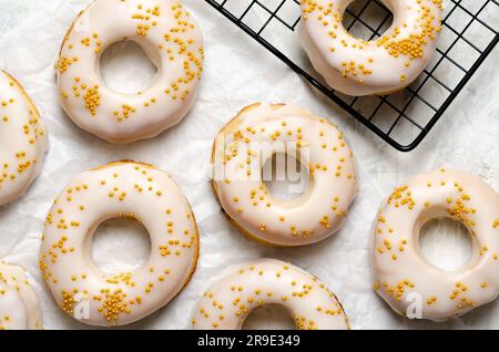 Hausgemachte, geeiste Donuts mit goldenen Perlen auf einem schwarzen Gestell und auf Backpapier. Stockfoto