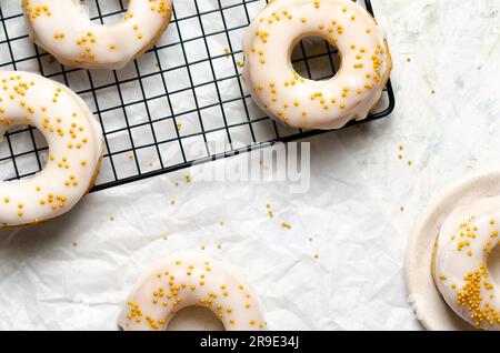 Hausgemachte, geeiste Donuts mit goldenen Perlen auf einem schwarzen Gestell und auf Backpapier. Stockfoto