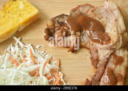 Gebratenes Schweinesteak mit Butter, Knoblauchbrot und Salat auf dem Schneidebrett Stockfoto