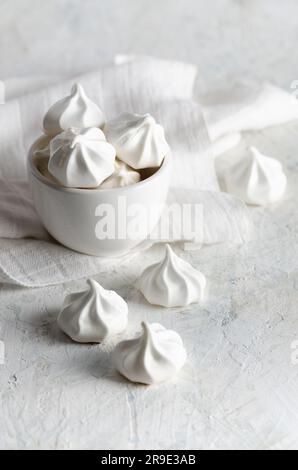 Weiße Meringue-Kekse in einer weißen Schüssel mit einer weißen Serviette, auf weißem Hintergrund. Stockfoto