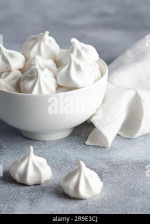 Weiße Meringue-Kekse in einer weißen Schüssel mit einer weißen Serviette, auf grauem Hintergrund. Stockfoto