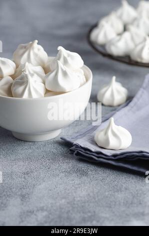 Weiße Meringue-Kekse in einer weißen Schüssel mit einer hellblauen Serviette, auf grauem Hintergrund. Stockfoto