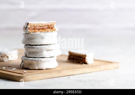 Weiße Alfajores gefüllt mit Dulce de leche auf einem Holzbrett und weißem Hintergrund. Stockfoto