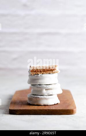 Weiße Alfajores gefüllt mit Dulce de leche auf einem Holzbrett und weißem Hintergrund. Stockfoto