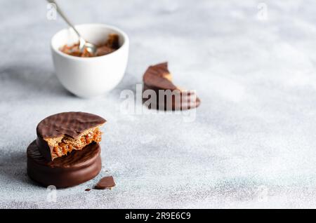 Dunkle Schokoladenalfajores und eine Schüssel mit Dulce de leche auf grauem Hintergrund. Stockfoto