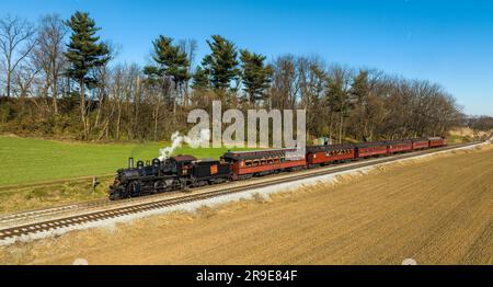 Ronks, Pennsylvania, 26. November 2022 - A Drone View of a restaurated Steam Passenger Train Traveling Thru Farmlands, die zu einer kleinen Station fahren Stockfoto