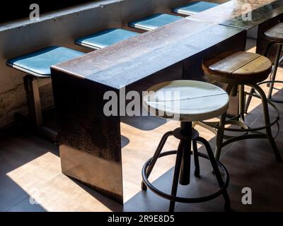 Nahaufnahme leere runde drehbare Holzstühle, stilvoller Tisch und lange Sitzreihe aus Eisen und Holz, im Loftstil dekoriert in einem Café oder Restaurant in der Nähe Stockfoto