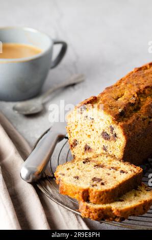 Eine Tasse Kaffee und ein Stück Bananenbrot mit Schokoladenchips auf grauem Hintergrund. Stockfoto