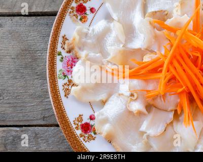 Frischer Muschel-Sashimi. Nahaufnahme weiße rohe Riesenmurex Murex Muscheln Fleisch dekoriert mit geriebenen Karotten auf dem runden Teller, traditioneller asiatischer Patt Stockfoto