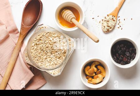 Haferflocken, Honig, Nüsse und getrocknete Preiselbeeren auf weißem Marmorhintergrund. Stockfoto