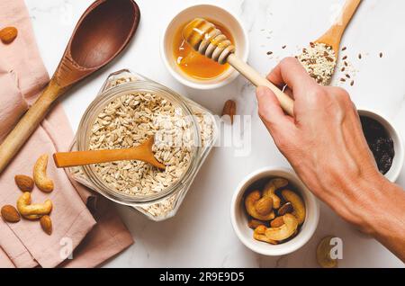 Haferflocken, Honig, Nüsse und Holzlöffel auf weißem Marmorhintergrund. Stockfoto
