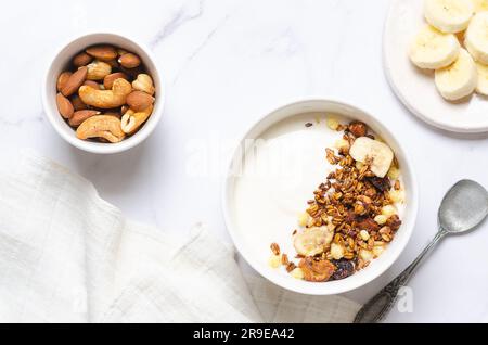 Gesundes Frühstück mit Joghurt, Müsli und Nüssen auf weißem Hintergrund. Stockfoto