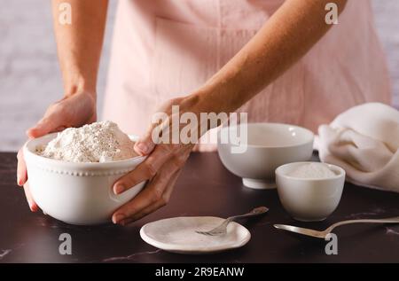 Nahaufnahme von weiblichen Händen, die eine Schüssel Mehl zum Kneten halten. Kochprozess. Stockfoto