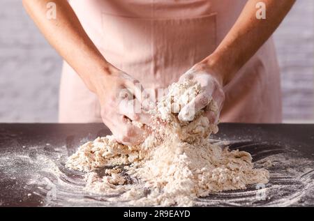 Weibliche Hände kneten Teig auf einem Tisch in der Küche, Nahaufnahme. Kochprozess. Stockfoto