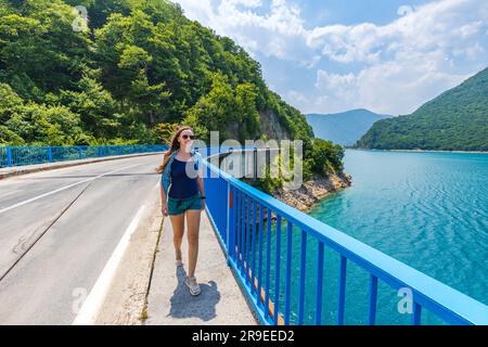 Junge Frau, die auf der Brücke über den Piva-See in Montenegro spaziert Stockfoto