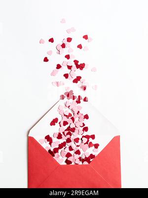 Roter Papierumschlag mit roten und pinkfarbenen Valentinsherzen auf weißem Hintergrund. Flach liegend, Draufsicht. Romantischer Liebesbrief für Valentinstagskonzept. Stockfoto