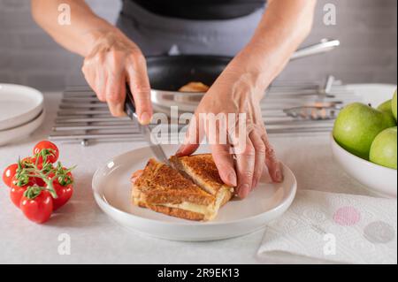 Schinken-Käse-Sandwich wird von Frauen mit einem Messer in zwei Hälften geschnitten Stockfoto