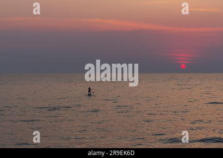 Einsamer SUP-Boardman, Surfer segelt auf dem Meerwasser in Richtung untergehende Sonne, Abenteuer auf dem Meer. Silhouette männlicher Tourist auf dem Paddle Board unter Trop Stockfoto