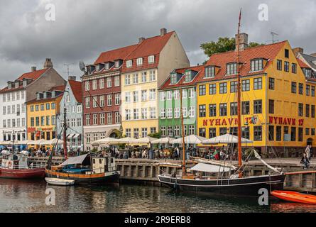 Kopenhagen, Dänemark - 14. September 2010: Kurzer Abschnitt der farbigen Fassaden der Nyhavn Restaurantreihe und viele Menschen. Kleine Boote auf dem Wasser und graue C. Stockfoto