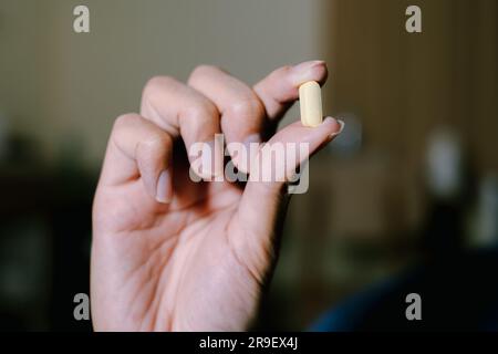 Eine gelbe Pille wird durch Zeigen gehalten und Daumenfinger mit drei anderen Fingern sind unten. Isolierter schwarzer Hintergrund. Geeignet für Werbung. Stockfoto