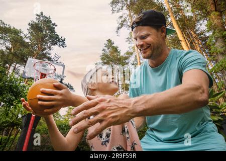 Vater und Tochter spielen Basketball im Hinterhof. Aktive Familie, die Spaß hat und Zeit miteinander verbringt Stockfoto