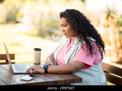 Seitenansicht einer jungen hispanischen Dame, die draußen auf dem Laptop tippt Stockfoto