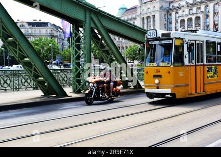 Budapest, Juni 2023: Harley Davidson Motorcycle Festival. HD120 Jahre. Radfahrer fahren auf der Liberty Bridge. Gelbe Straßenbahn. Das Geller Hotel ist weit weg. Stockfoto