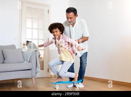 Senior Grandpa unterrichtet Enkel, wie man zu Hause Skateboard fährt Stockfoto