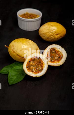 Eine weiße Keramikschüssel, die bis zum Rand mit Passionsfrucht auf schwarzer Oberfläche gefüllt ist Stockfoto