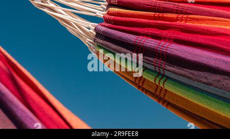 Nahaufnahme von zwei regenbogenfarbenen Hängematten vor dem blauen Himmel Stockfoto