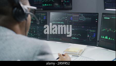Der afroamerikanische Aktienhändler kommuniziert mit dem Anlageberater über Echtzeit-Aktien und Börsenkurse-Diagramme auf dem Computer. Geschäftsleute arbeiten im Maklerbüro. Investitionen und Analysen. Stockfoto