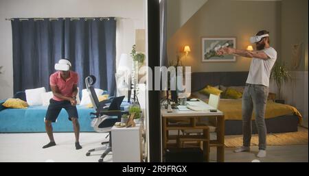 Ethnische Männer und Nachbarn in VR-Headsets spielen Augmented-Reality-Videospiele mit Wireless-Controllern. Blick auf zwei durch Wände getrennte Zimmer oder Apartments. Konzept von Nachbarschaft und Lebensstil. Stockfoto