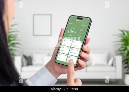 Frau verwendet Smart-Home-App auf Smartphone. Wohnzimmereinrichtung im Hintergrund. Hausautomatisierungskonzept Stockfoto