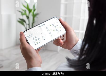 Modernes Leben als Frau verwaltet mühelos ihr intelligentes Zuhause über ein Mobiltelefon und den Hintergrund des Wohnzimmers Stockfoto