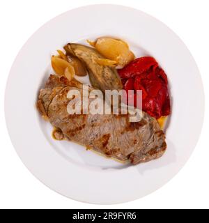 Auf dem runden weißen Teller liegt eine saftige gebratene Scheibe Rinderfilet, garniert mit gedünstetem Gemüse. Stockfoto