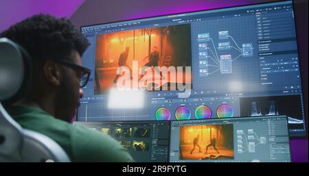 Rückansicht eines afroamerikanischen Redakteurs, der Farbkorrektur macht, im Heimstudio arbeitet. Actionfilmaufnahmen und Software-Schnittstelle auf Computer und großem digitalen Bildschirm. Das Konzept der Filmpostproduktion. Stockfoto