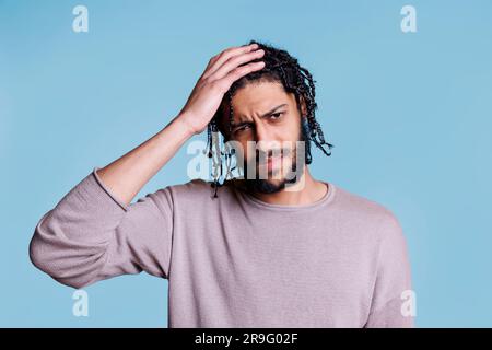 Ein müder araber, der Kopfschmerzen hat, den Nacken berührt und in die Kamera schaut. Erschöpfter junger, gutaussehender Mensch, der Hand am Kopf hält und Gesichtsgrimace macht, während er an Migräne leidet Stockfoto